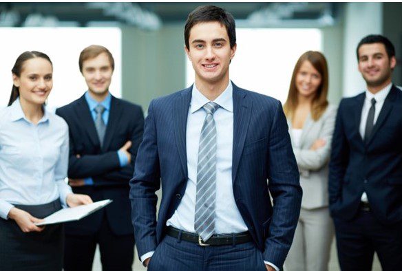 A man in suit and tie standing next to other people.