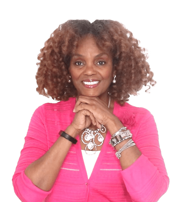 A woman with curly hair and pink jacket holding her hands in front of her face.